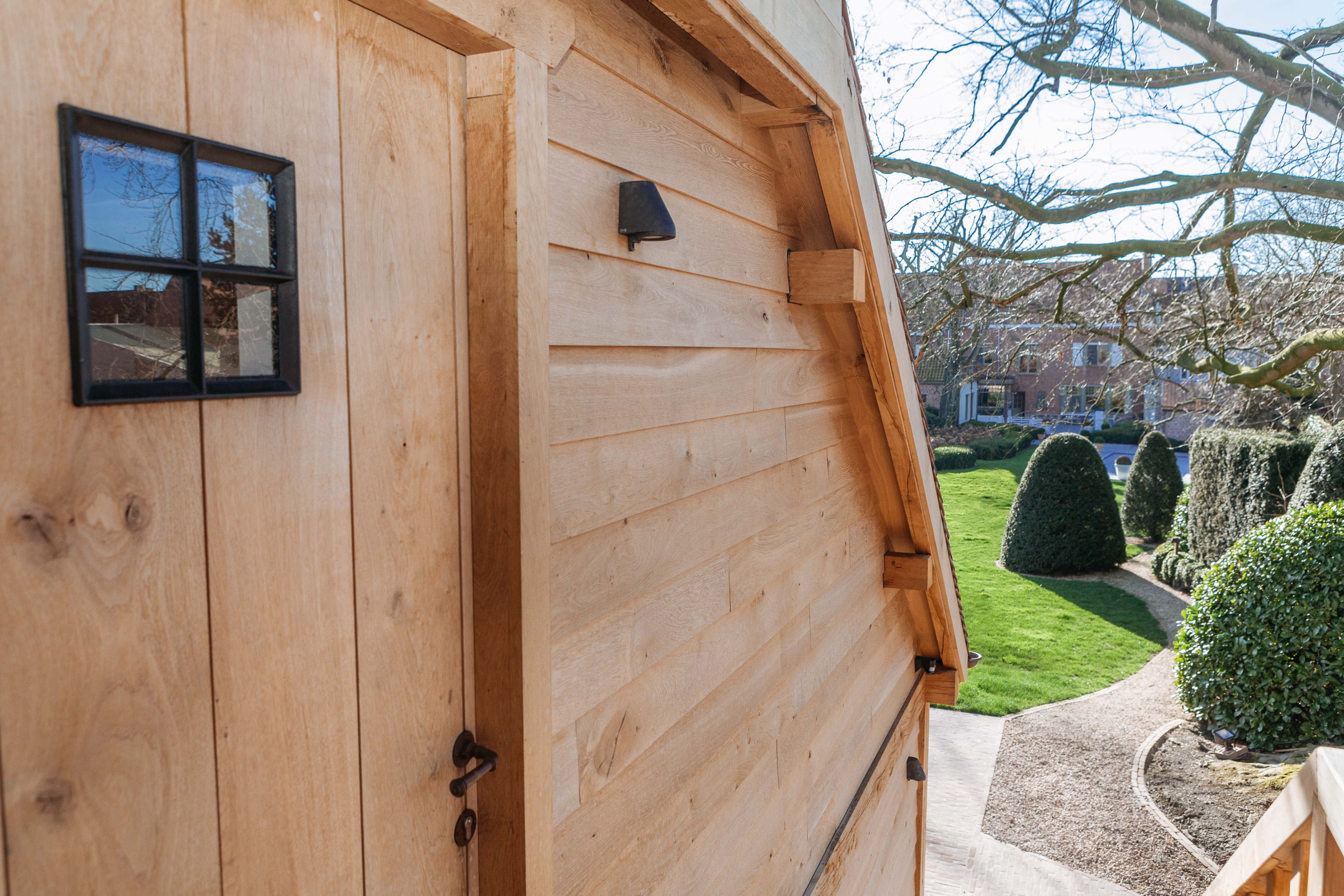 Eiken wand met stalen raam van eikenhouten carport met guest house - Vanhauwood in samenwerking met Cornelis Hout Deze eiken wand behoort tot een rustieke eiken carport met guesthouse. Dit eikenhouten bijgebouw werd gerealiseerd door Vanhauwood. Voor de opbouw van de structuur maakten ze gebruik van een op maat gemaakt eiken bouwpakket van Cornelis Hout.