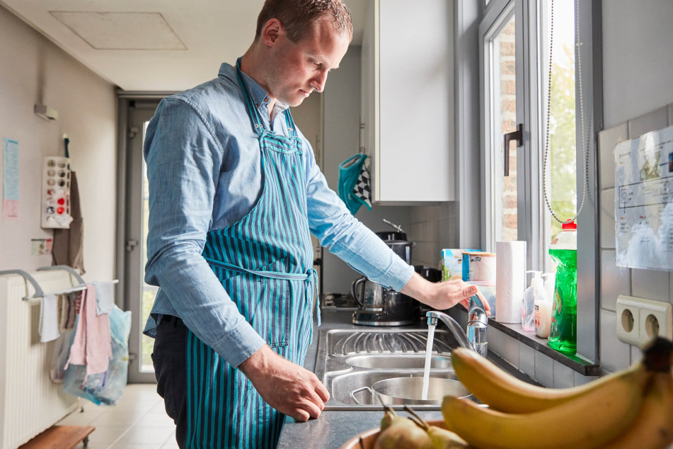 Jonge man met beperking staat in keuken met schort aan
